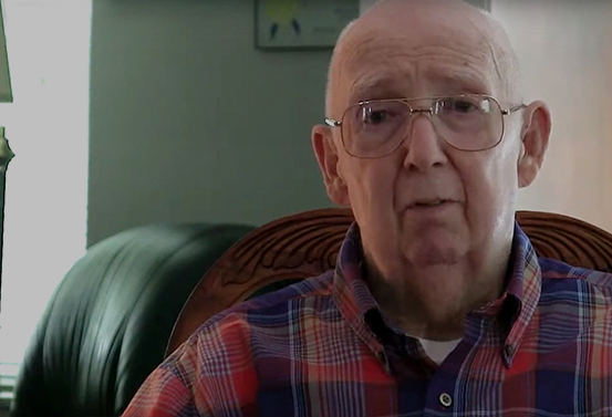 Elder man with plaid shirt speaking to a camera.